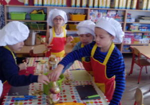 Dzieci wkładają pokrojone kawałki jabłka do słoików.